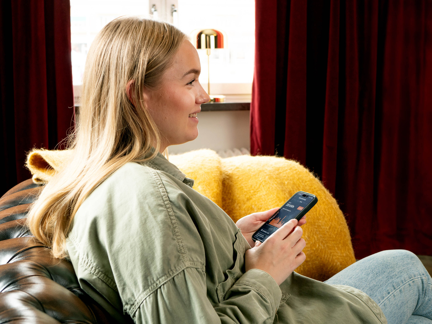Leende kvinna sitter i soffan och använder sin mobiltelefon.
